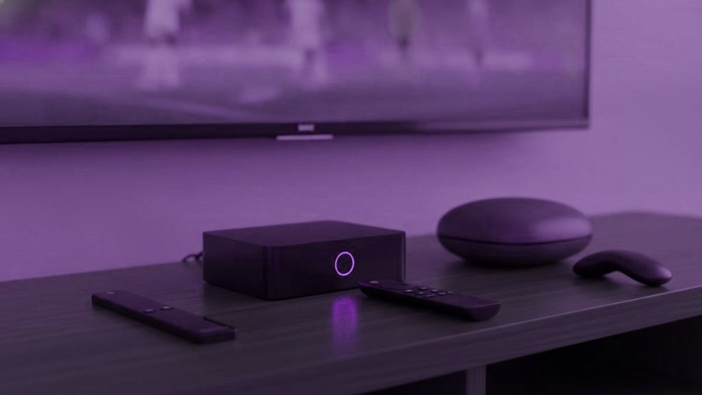A streaming stick, a set-top box and a round streaming box with their remotes on a TV console