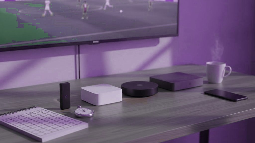 Five streaming devices, a notebook scoring grid and a stopwatch in front of a TV showing a football match
